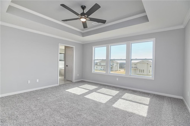 spare room featuring a tray ceiling, carpet, crown molding, and baseboards