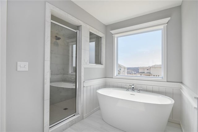 bathroom with a wainscoted wall, a freestanding tub, and a stall shower