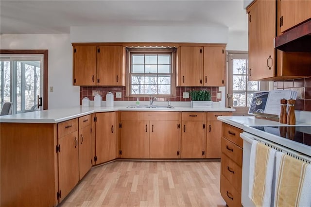 kitchen with white electric range oven, a peninsula, a sink, light countertops, and under cabinet range hood