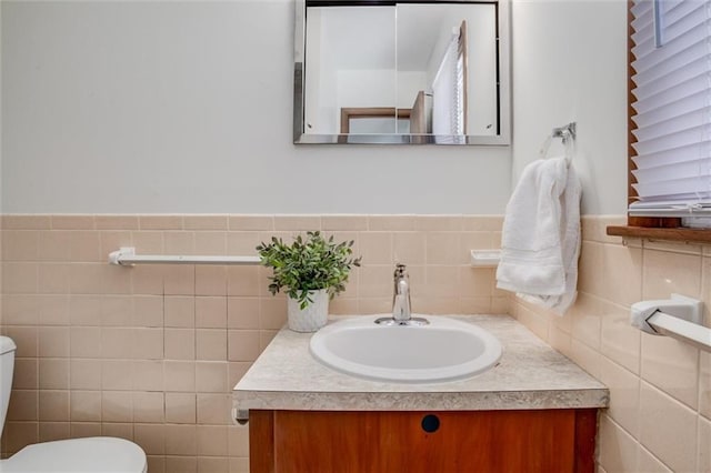 half bath featuring tile walls, wainscoting, toilet, and vanity