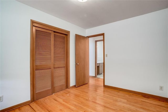 unfurnished bedroom featuring light wood finished floors, baseboards, and a closet