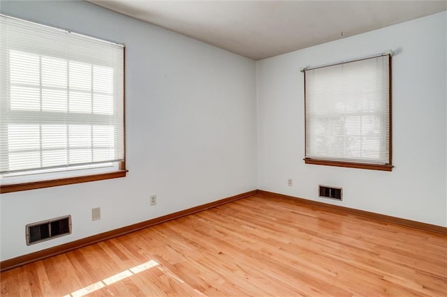 empty room with light wood-style floors, visible vents, and baseboards