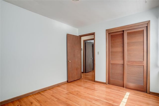 unfurnished bedroom featuring light wood finished floors, a closet, and baseboards