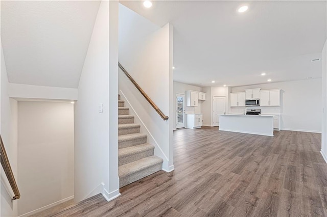 unfurnished living room with baseboards, stairway, wood finished floors, and recessed lighting