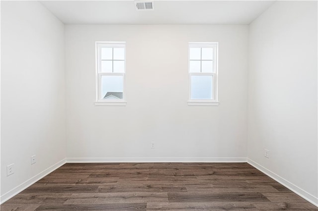 spare room featuring dark wood-style flooring, visible vents, and baseboards