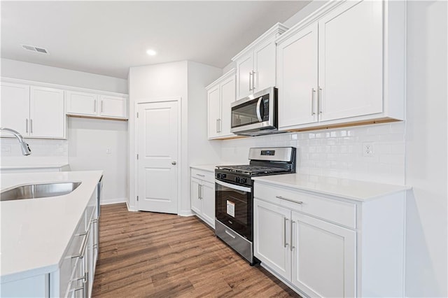 kitchen with stainless steel appliances, backsplash, white cabinets, a sink, and wood finished floors