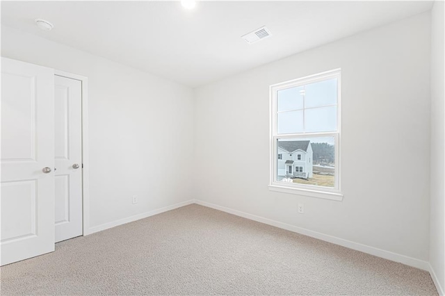 spare room featuring light carpet, visible vents, and baseboards