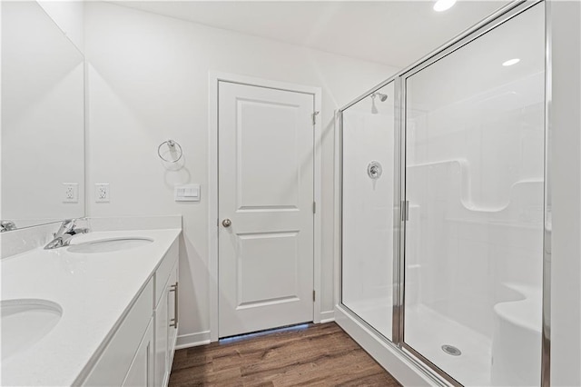 full bath with double vanity, wood finished floors, a sink, and a shower stall