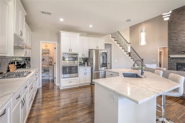 kitchen featuring visible vents, dark wood-style flooring, a sink, stainless steel appliances, and backsplash