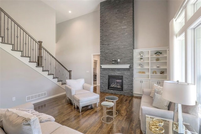 living area with a stone fireplace, a high ceiling, wood finished floors, visible vents, and stairs