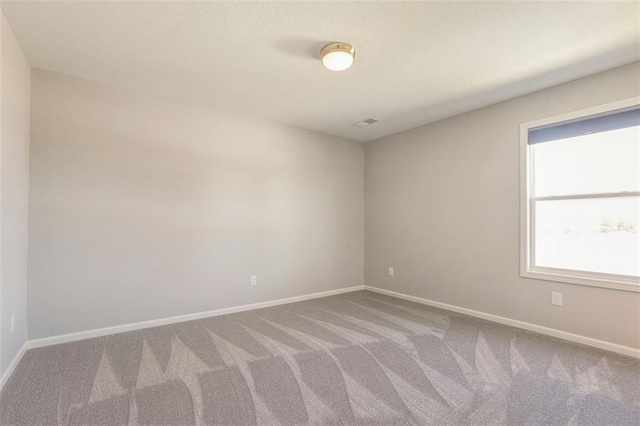 carpeted spare room featuring a textured ceiling and baseboards