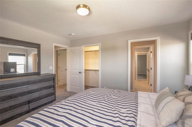 bedroom with a textured ceiling, a spacious closet, a closet, and dark carpet