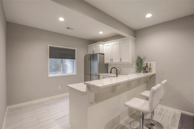 kitchen with visible vents, white cabinets, freestanding refrigerator, tasteful backsplash, and a kitchen bar