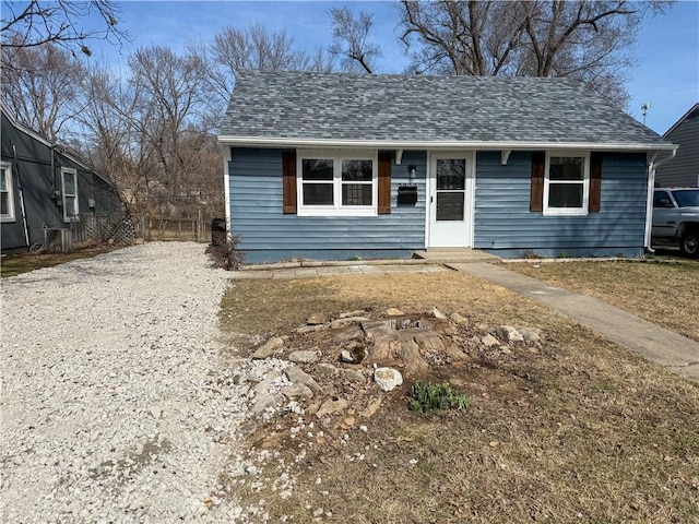 view of front facade with a shingled roof, gravel driveway, and fence