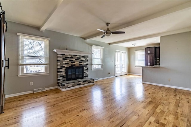 unfurnished living room featuring a fireplace, light wood finished floors, visible vents, ceiling fan, and beamed ceiling