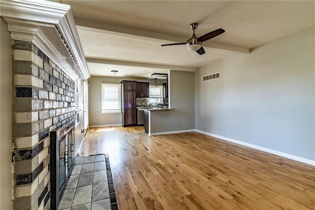 unfurnished living room with a fireplace, visible vents, light wood-style floors, beamed ceiling, and baseboards