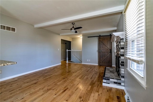 unfurnished living room featuring a barn door, baseboards, visible vents, beamed ceiling, and wood finished floors