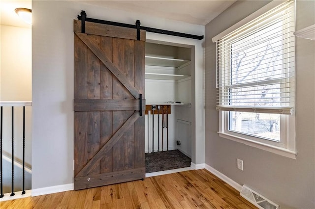 interior space featuring a barn door, wood finished floors, visible vents, and baseboards