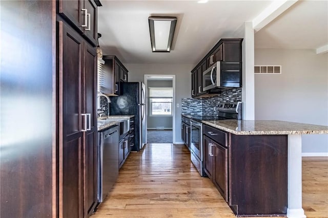 kitchen featuring light stone counters, backsplash, appliances with stainless steel finishes, light wood-style floors, and dark brown cabinets