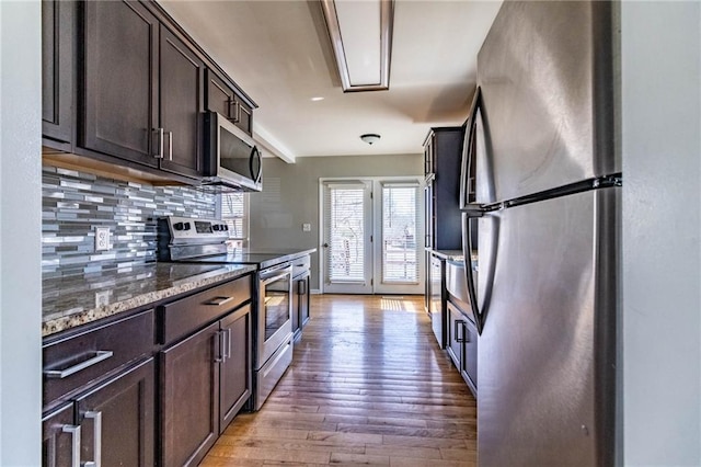 kitchen featuring dark brown cabinetry, stone counters, stainless steel appliances, and backsplash