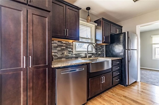 kitchen with dark brown cabinetry, stainless steel appliances, a sink, light wood-type flooring, and backsplash