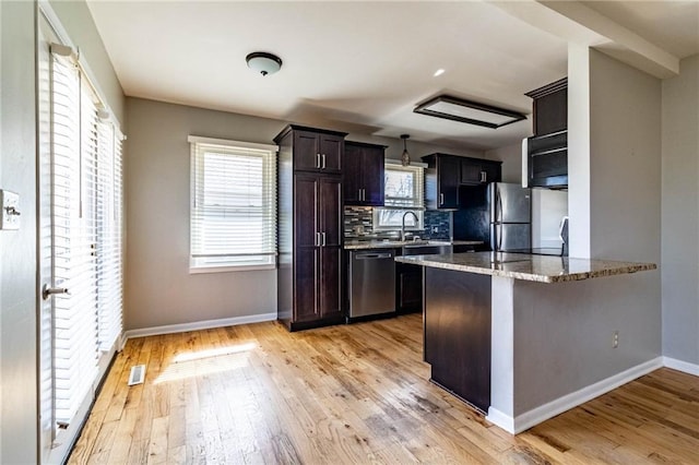 kitchen with stone counters, a sink, stainless steel dishwasher, light wood-type flooring, and freestanding refrigerator