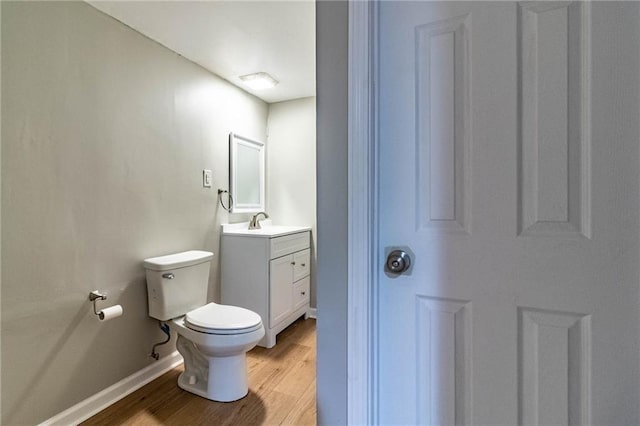 half bath with toilet, baseboards, wood finished floors, and vanity