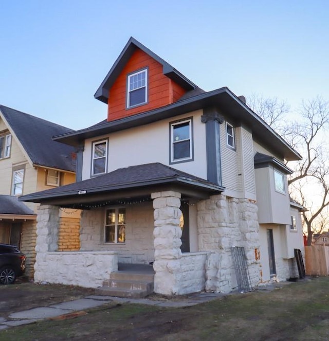 american foursquare style home featuring a porch and stone siding