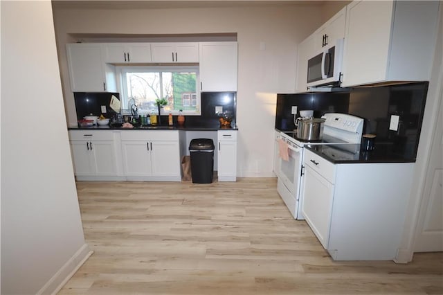 kitchen featuring light wood finished floors, white appliances, dark countertops, and white cabinetry