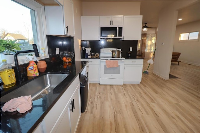 kitchen featuring light wood finished floors, electric stove, stainless steel microwave, white cabinetry, and a sink