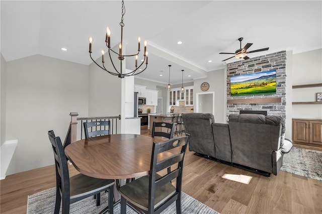 dining area featuring ornamental molding, light wood-style flooring, ceiling fan with notable chandelier, a fireplace, and lofted ceiling