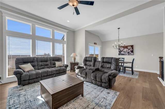 living room featuring wood finished floors, baseboards, ornamental molding, vaulted ceiling, and ceiling fan with notable chandelier