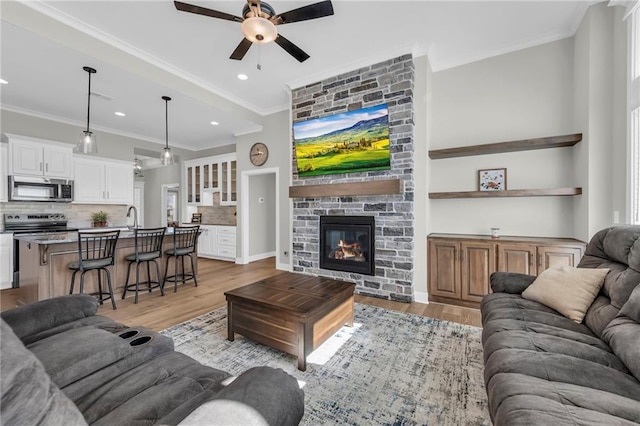 living area with light wood-style flooring, a large fireplace, a ceiling fan, and ornamental molding