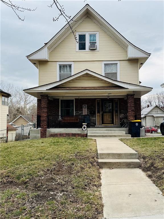 american foursquare style home with brick siding, a front lawn, fence, and covered porch