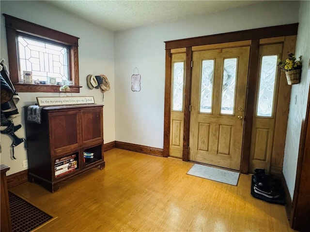 foyer entrance featuring light wood-style flooring, a textured ceiling, and baseboards