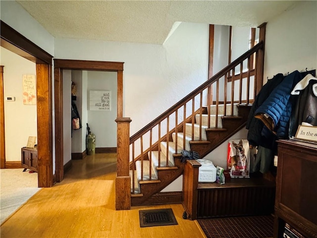 staircase featuring wood finished floors, baseboards, visible vents, and a textured ceiling