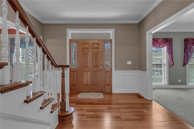 foyer entrance featuring stairs, light wood-type flooring, ornamental molding, wainscoting, and a decorative wall