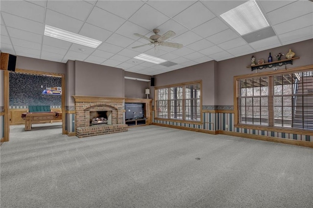 unfurnished living room with carpet flooring, a brick fireplace, ceiling fan, and a drop ceiling