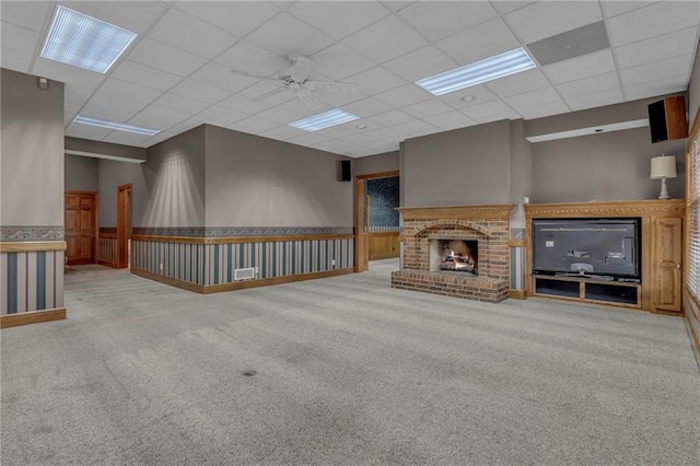 unfurnished living room featuring visible vents, carpet floors, a fireplace, a drop ceiling, and ceiling fan