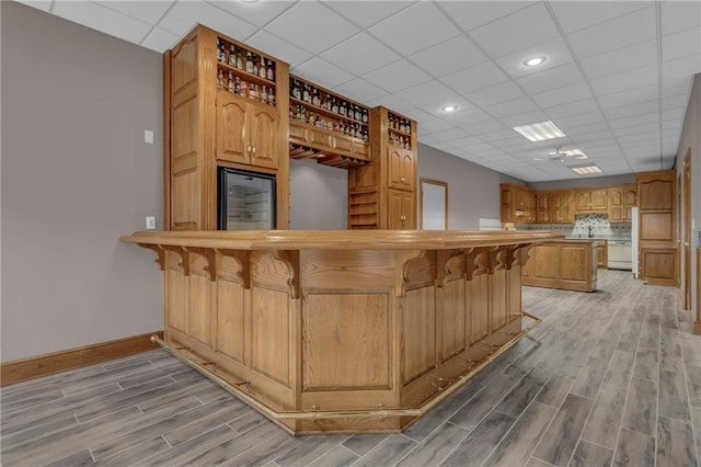 kitchen featuring baseboards, wood finish floors, a drop ceiling, a kitchen bar, and open shelves