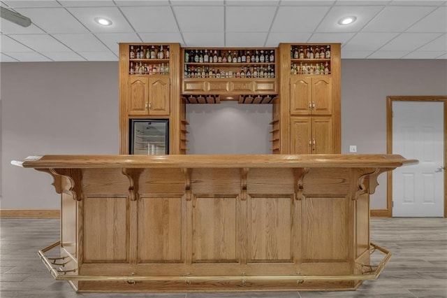 bar featuring fridge, baseboards, light wood-style floors, a bar, and a paneled ceiling