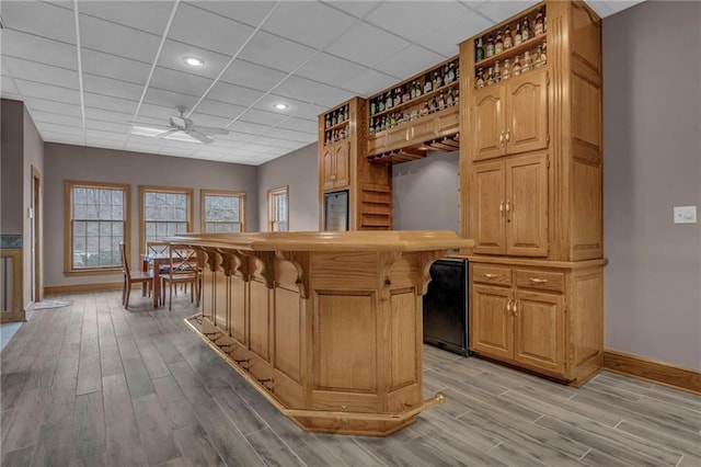 interior space with ceiling fan, baseboards, a dry bar, light wood-style floors, and a paneled ceiling