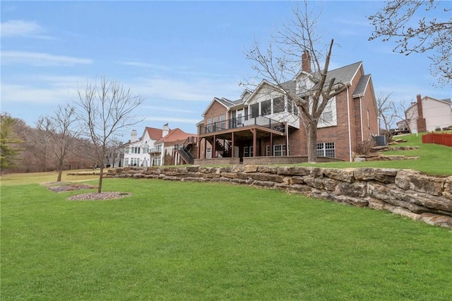 back of house with stairway, a wooden deck, a chimney, a lawn, and brick siding