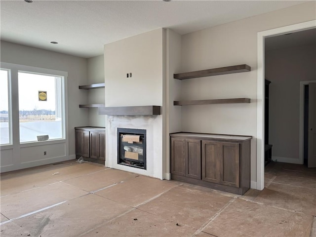 unfurnished living room with a glass covered fireplace and baseboards