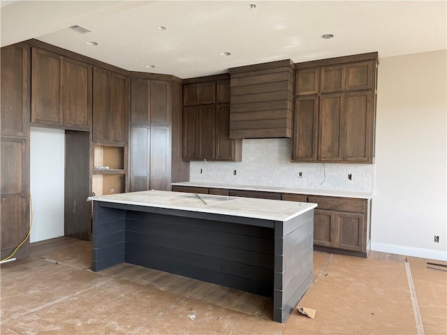kitchen featuring visible vents, a kitchen island, tasteful backsplash, light countertops, and baseboards