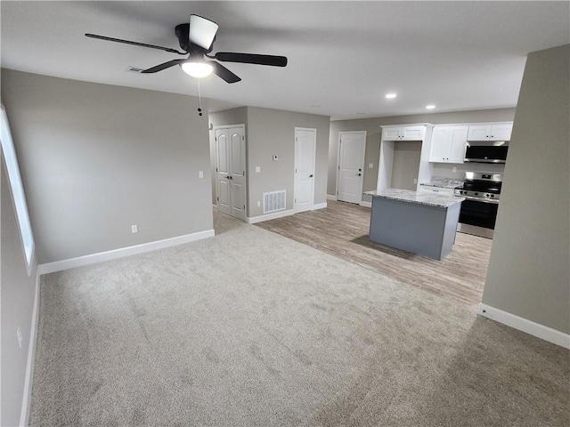 kitchen with light carpet, stainless steel appliances, visible vents, white cabinets, and baseboards