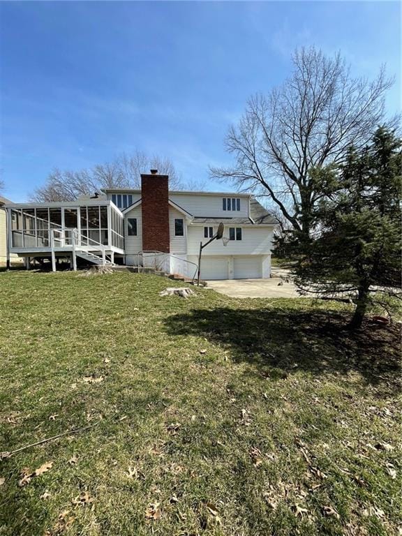 rear view of house featuring driveway, a lawn, a sunroom, a chimney, and an attached garage