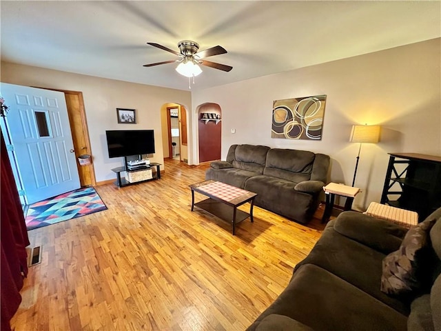 living room with arched walkways, ceiling fan, light wood-style flooring, visible vents, and baseboards