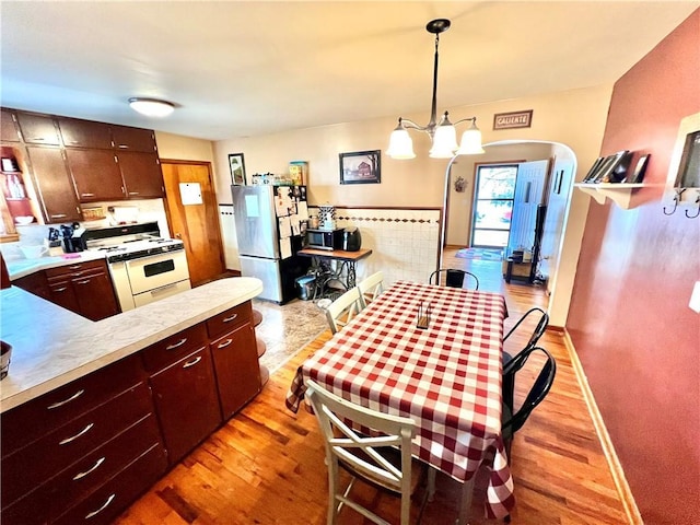 kitchen with arched walkways, light countertops, light wood-style floors, freestanding refrigerator, and white gas range oven