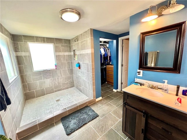 bathroom featuring tile patterned flooring, a tile shower, vanity, and a spacious closet